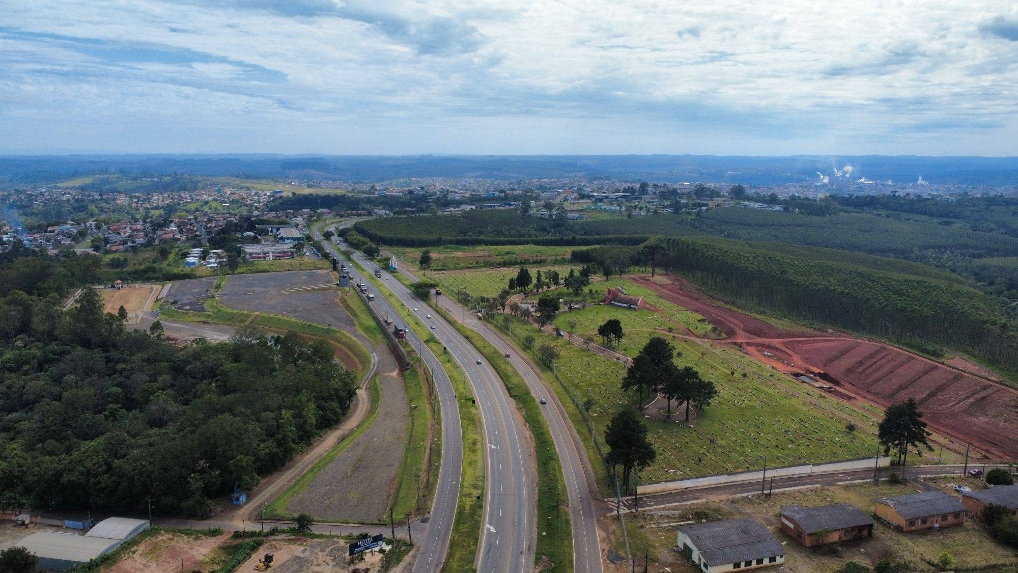 Vista aérea de Telêmaco Borba (PR): rodovia duplicada no acesso à cidade, a área urbana ao fundo e áreas de reflorestamento em volta
